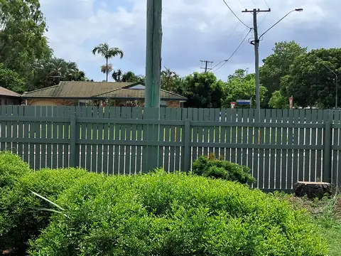 A long timber fence painted sage green behind a green hedge